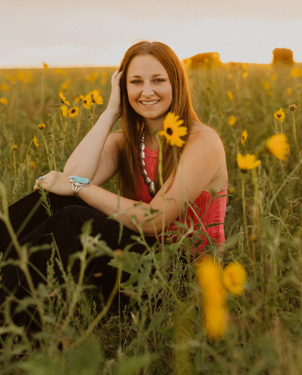 Charley sits in field surrounded by sunflowers for her senior picture.